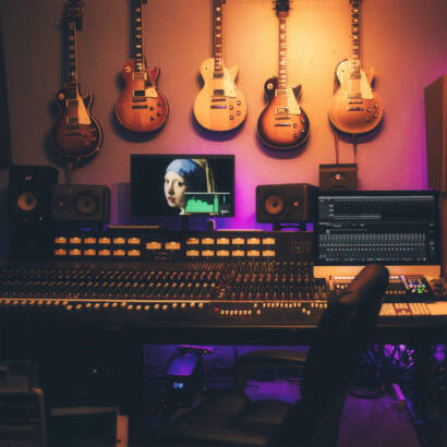 A room with guitars hanging on the wall and a person in front of a monitor.