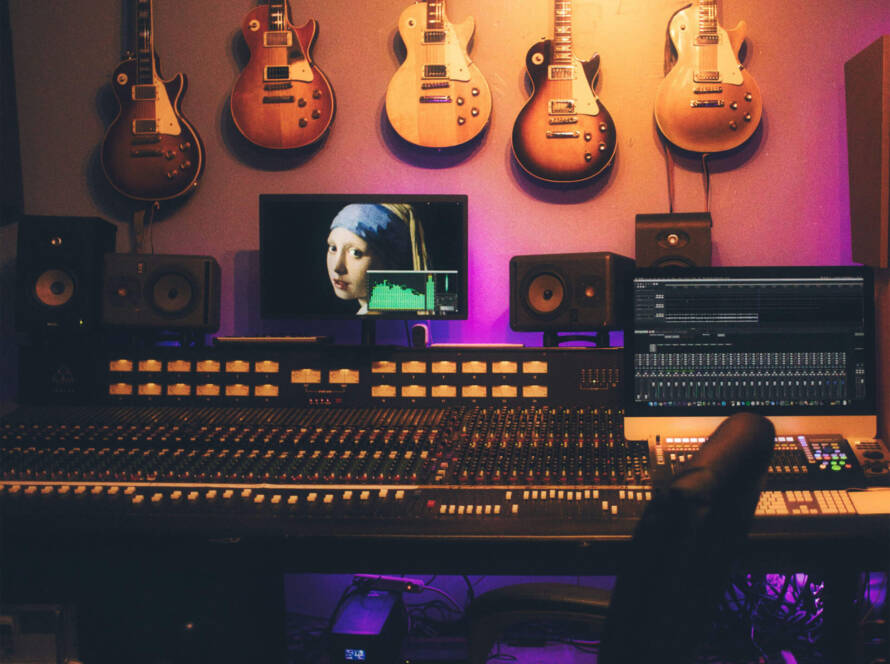 A room with guitars hanging on the wall and a person in front of a monitor.