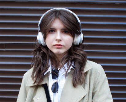 A woman wearing headphones and a trench coat.