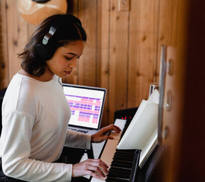 A girl is playing the piano in front of her laptop.