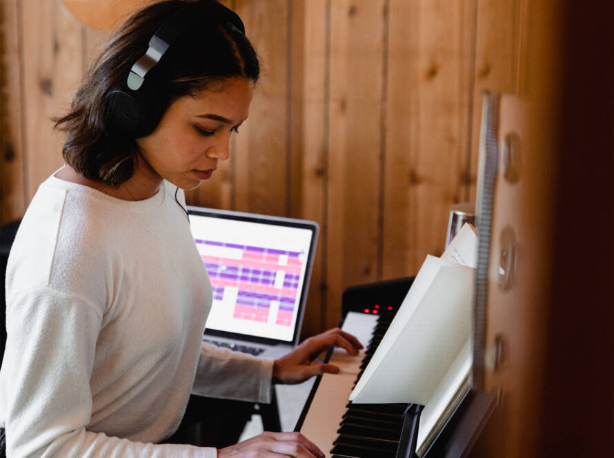 A girl is playing the piano in front of her laptop.