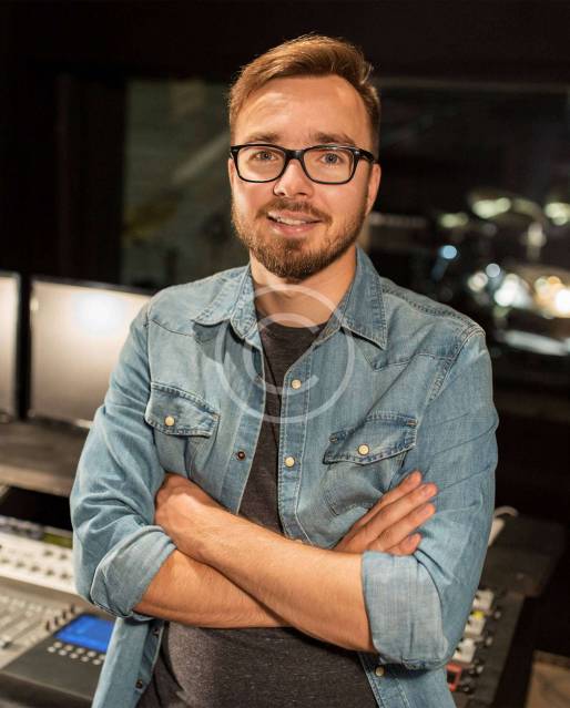 A man with his arms crossed in front of a sound board.