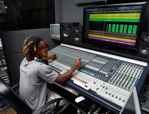 A man sitting at a mixing desk in front of a large monitor.